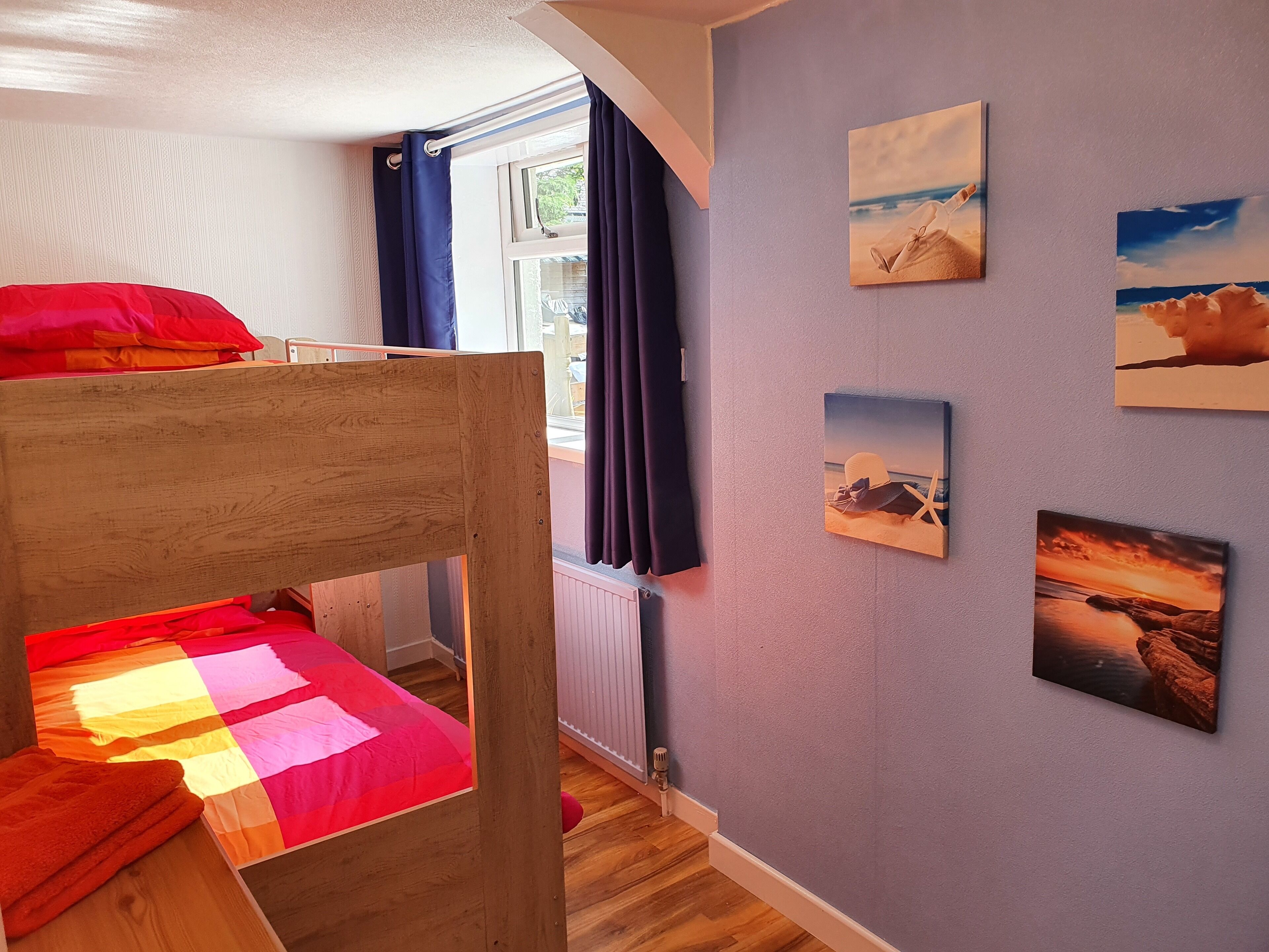 Une chambre avec un lit superposé, une fenêtre avec des rideaux et des œuvres d’art murales représentant des paysages.