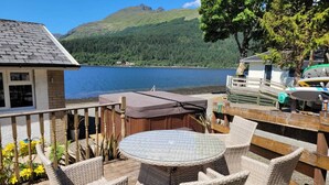 Eine Terrasse mit Korbmöbeln und einem Glastisch mit Blick auf einen See und bewaldete Hügel.
