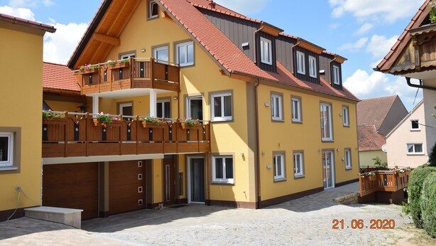A yellow building with a red roof, a wooden balcony with flowers, and a garage.