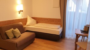 A hotel room with a wooden headboard bed, a brown sofa with cushions, a small wooden table, and a wall-mounted lamp.