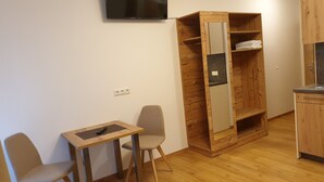 A small kitchenette with a wooden cabinet, a TV mounted on the wall, and a table with chairs.
