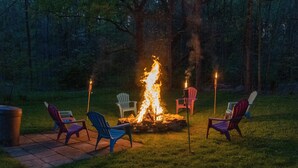 A fire pit surrounded by Adirondack chairs in a grassy area with trees in the background. - Lakeside living awaits at beautiful Lake Milton, OH
 with dock across the street (Lake Milton)