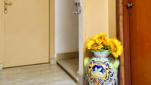 A hallway with a wooden door, a wall-mounted camera, a decorative seahorse, and a vase with sunflowers. - Hippocampus B&B (Giardini Naxos)
