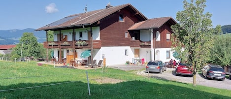 A two-story house with a balcony, a garden, and a car parked in front.
