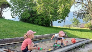 Deux enfants jouent dans un bac à sable avec des jouets et une pelle.