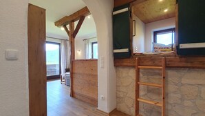 Ein Zimmer mit einer Steinwand, Holzbalken, einer Leiter und einem Fenster mit Blick.