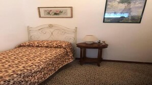 Een slaapkamer met een bedovertrek met patroon, een klein nachtkastje met een lamp, en twee ingelijste foto's aan de muur.