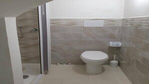 Een badkamer met toilet, douche en betegelde wand.