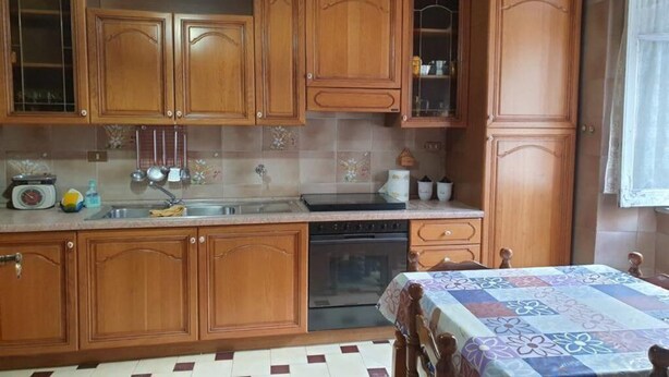 Een keuken met houten kastjes, een spoelbak, een fornuis en een tafel met een tafelkleed met een patroon.