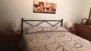 Een slaapkamer met een bed, nachtkastje, dressoir en een schilderij aan de muur.