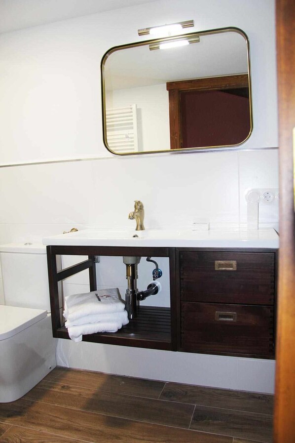 A bathroom with a white sink, dark wooden vanity, and a mirror above the sink. - O Yunque - Casa Ferrador (Ribeira Sacra) (Bolmente)