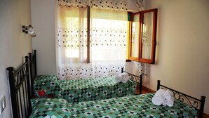 Ein Zimmer mit zwei Betten, jeweils mit karierten, grün-weißen Bettdecken, einem spiegelnden Holzrahmen und einem Fenster mit gemusterten Vorhängen.