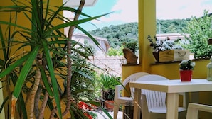 Eine Terrasse mit einem Blumentopf, einem weißen Kunststoffstuhl und einem Tisch mit einem roten Topf.