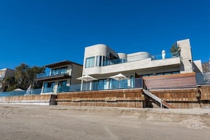 A modern building with a curved facade, large windows, and a wooden deck with umbrellas.