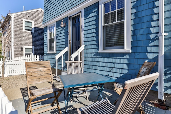 A blue house with a white picket fence, a wooden bench, and a metal table.