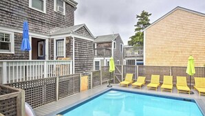 Ein Schwimmbecken mit gelben Liegestühlen und Sonnenschirmen, umgeben von Holzhäusern, einer Holzterrasse und einem Zaun.