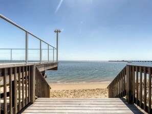 A wooden boardwalk leading to a beach with a clear view of the ocean and a pier in the distance.