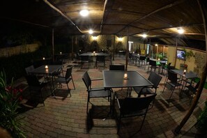 An outdoor patio with tables and chairs, a thatched roof, and a stone wall. - Agriturismo La Posta Reale (Castiglion Fibocchi)