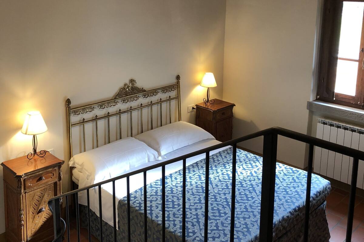 Ein Schlafzimmer mit einem Bett, zwei Nachttischen, einer Pendelleuchte, einem Fenster und einer Heizung.