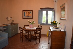 A dining area with a wooden table and chairs, a window with blue shutters, and a kitchen area with a sink and cabinets. - Agriturismo La Posta Reale (Castiglion Fibocchi)
