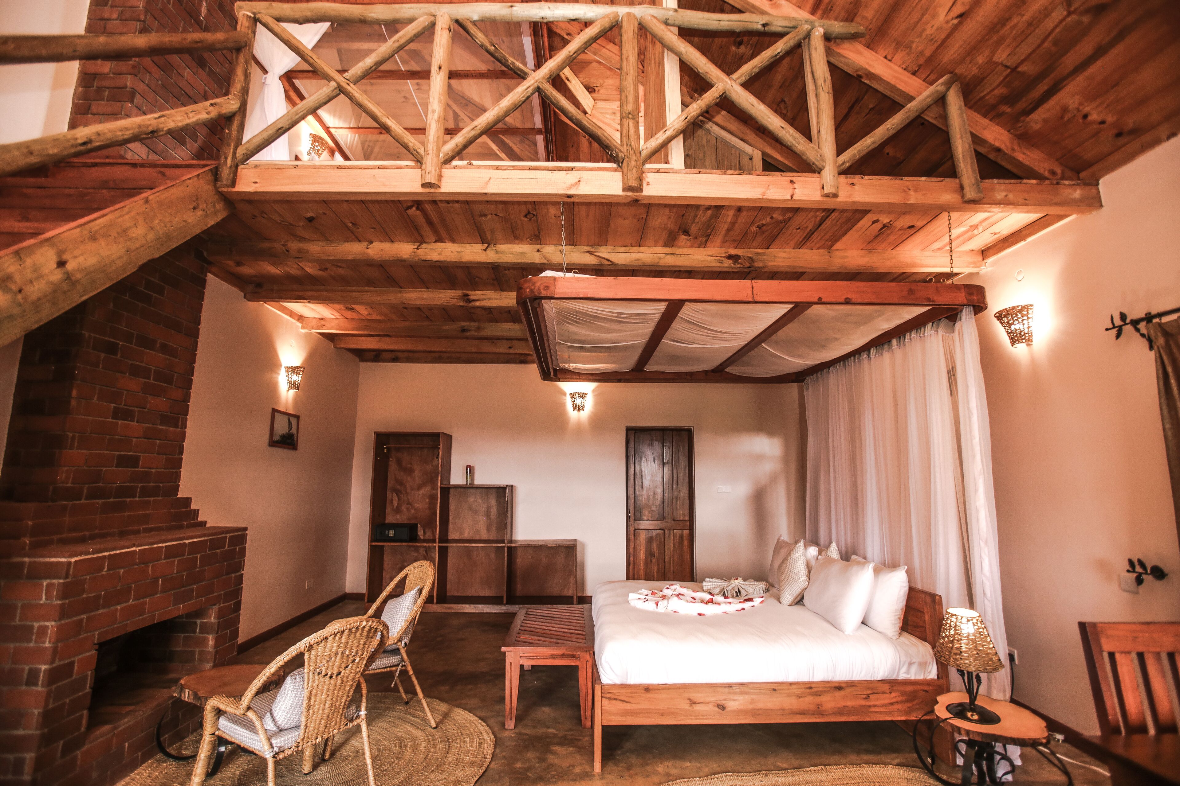 A rustic wooden room with a bed, a chair, a small table, and a fireplace.