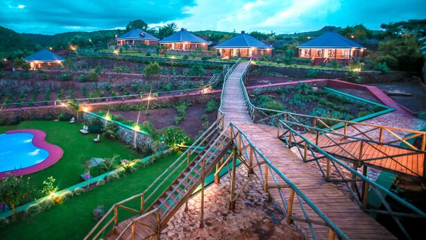 Un resort con varias villas conectadas por un puente de madera, una piscina y jardines ajardinados.