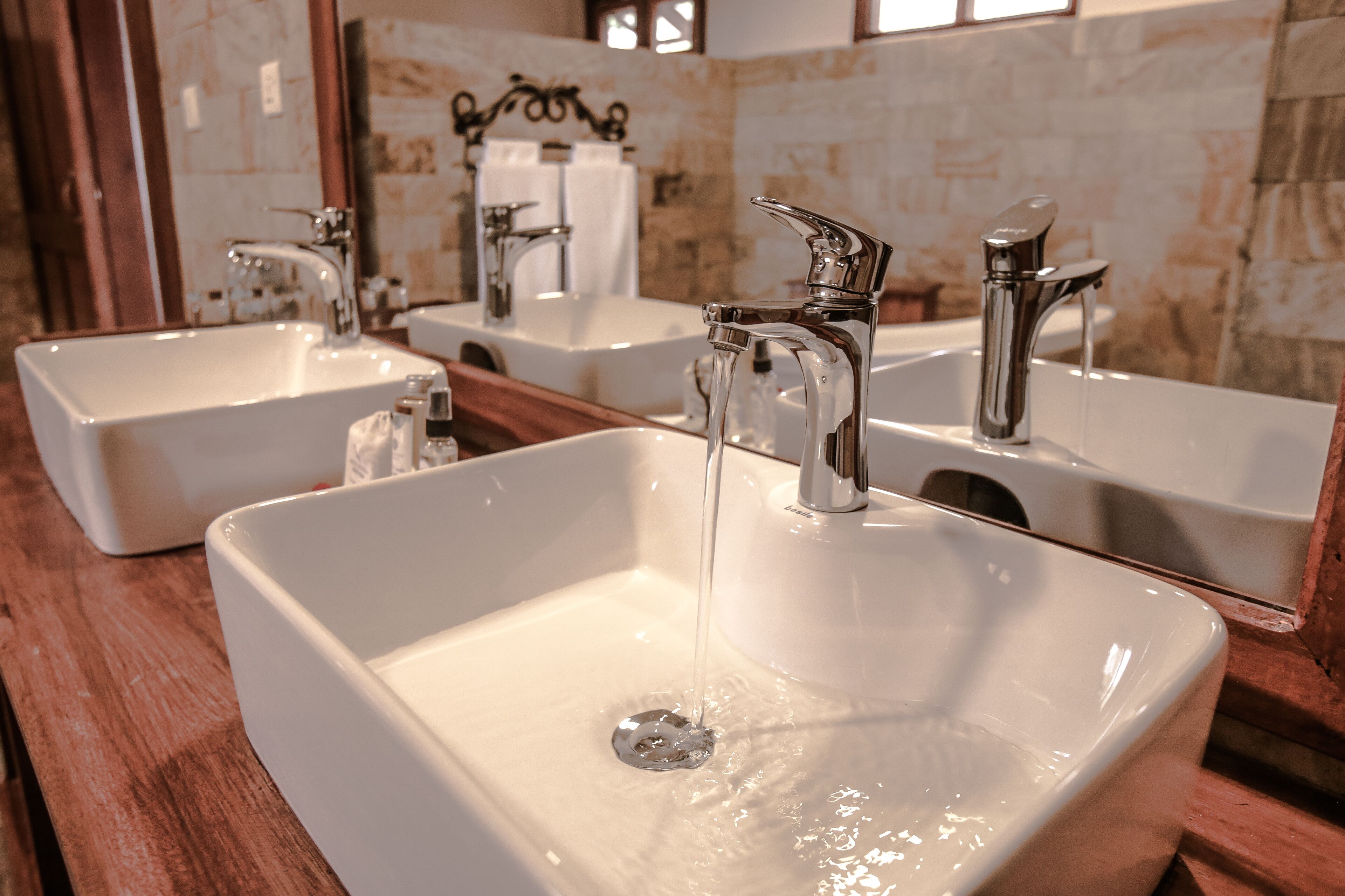 Ein Badezimmer mit drei weißen Waschbecken, jeweils mit einem modernen Wasserhahn, und einem Spiegel darüber.