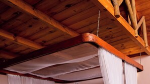 Un dormitorio con cama con dosel, vigas de madera en el techo y vistas al verdor exterior.
