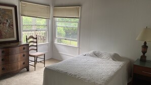 Un dormitorio con cama, cómoda, silla y ventanas.