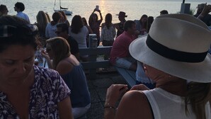 Un grupo de personas sentadas en un muelle, contemplando una puesta de sol sobre el agua.