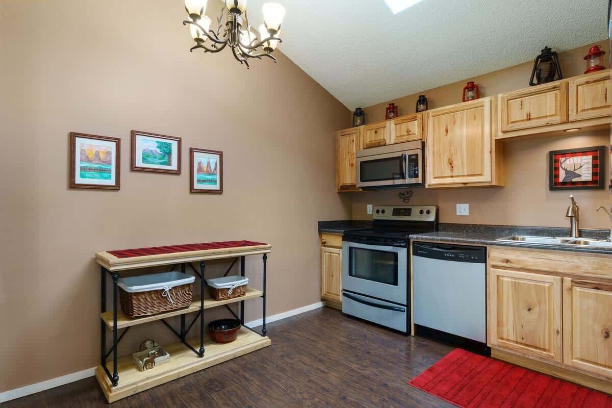 A kitchen with wooden cabinets, a microwave, an oven, and a dishwasher. There are three framed pictures on the wall and a red rug on the floor.