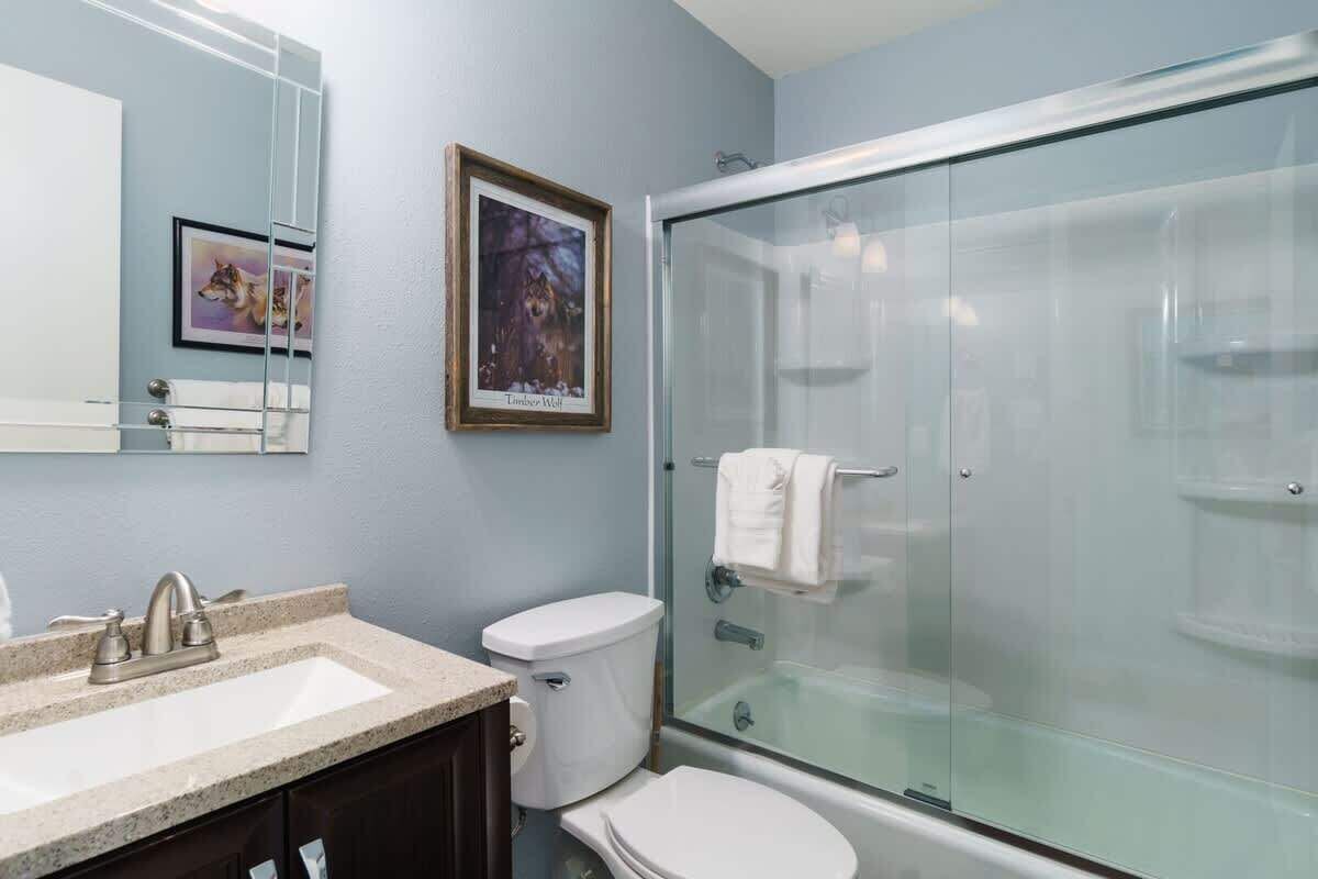 Une salle de bain avec une douche à parois de verre, un lavabo, des toilettes et des œuvres d’art encadrées accrochées au mur.