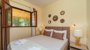 A neatly made bed with pillows and folded towels, a bedside table with a lamp, and a wall with decorative mirrors. - Holiday Home Sea - Two Bedroom Beach House (Petrovac)