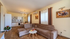 A modern living room with a beige sofa, a round coffee table, and a kitchen in the background. - Holiday Home Sea - Two Bedroom Beach House (Petrovac)