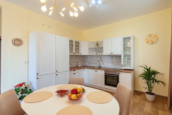 A modern kitchen with white cabinets, a marble countertop, and a dining area with a round table and placemats.