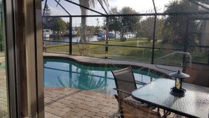 Une terrasse fermée par des baies vitrées, avec une piscine, une table et des chaises.