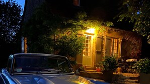 Un'auto d'epoca parcheggiata di fronte a una casa rustica con l'ingresso illuminato.