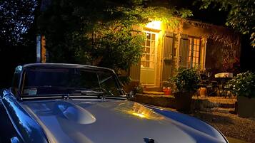 Un cotxe antic aparcat davant d'una casa rústica amb la porta d'entrada il·luminada.