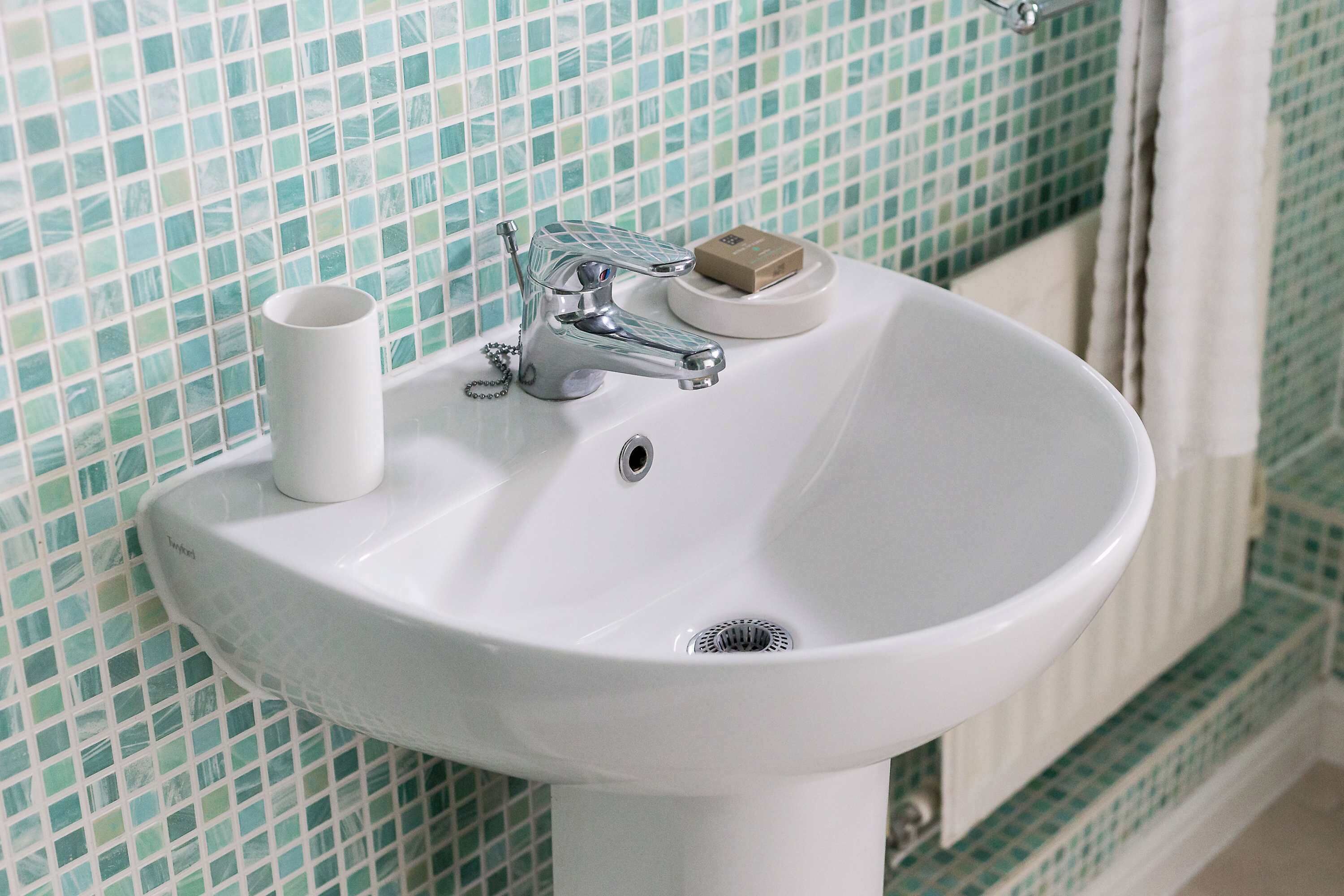A bathroom sink with a chrome faucet, a soap dish, and a toilet paper holder.
