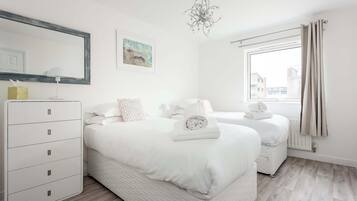 A modern bedroom with two beds, a dresser, a chandelier, and a window with curtains.
