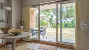 Ein Zimmer mit Esstisch, Stühlen, einem Ventilator und Blick auf einen Garten durch eine Schiebetür.