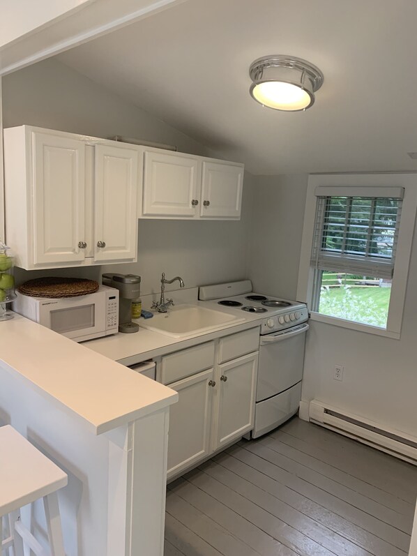 A kitchen with white cabinets, a microwave, a stove, and a window with blinds.