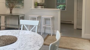 Une cuisine moderne avec des meubles blancs, une table à manger en marbre et une vue sur la salle à manger adjacente.