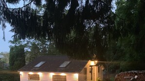 Une petite cabane à un seul étage, dotée d’un toit en pente, d’un porche et d’un chemin de pierre menant à l’entrée.