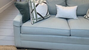 Une chambre à coucher avec un lit, une table de chevet avec une lampe, une fenêtre et un canapé gris avec des coussins.