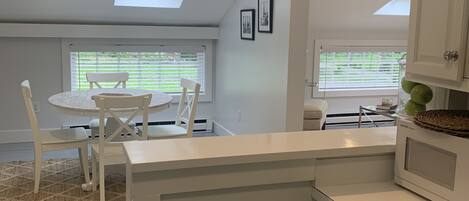 Eine moderne Küche mit weißen Schränken, ein Essbereich mit rundem Tisch und Stühlen, sowie Dachfenster für natürliches Licht.