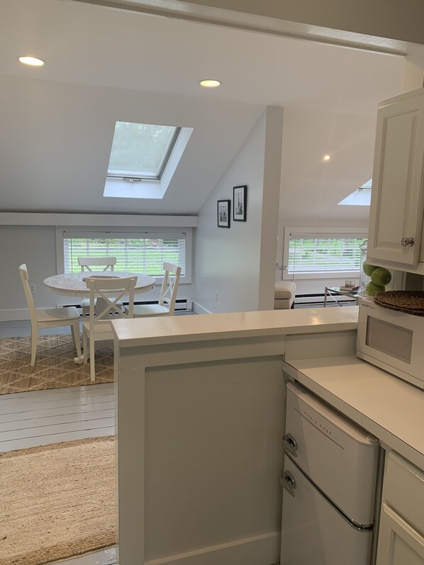 A modern kitchen with white cabinetry, a dining area with a round table and chairs, and skylights allowing natural light.