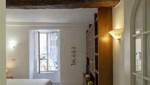 Een slaapkamer met een bed, een raam, een houten kast en een wandplank met decoratieve objecten.