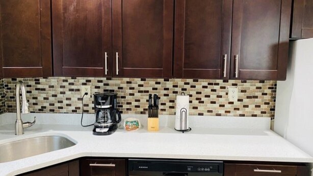 Een keuken met donkere houten kastjes, een wit aanrecht, een koffiezetapparaat, een keukenrolhouder en een vaatwasser.