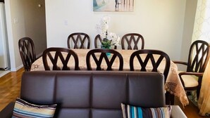 Een eethoek met een tafel voor vier personen, omringd door houten stoelen met een decoratief patroon. Boven de tafel hangt een schilderij van de Eiffeltoren.